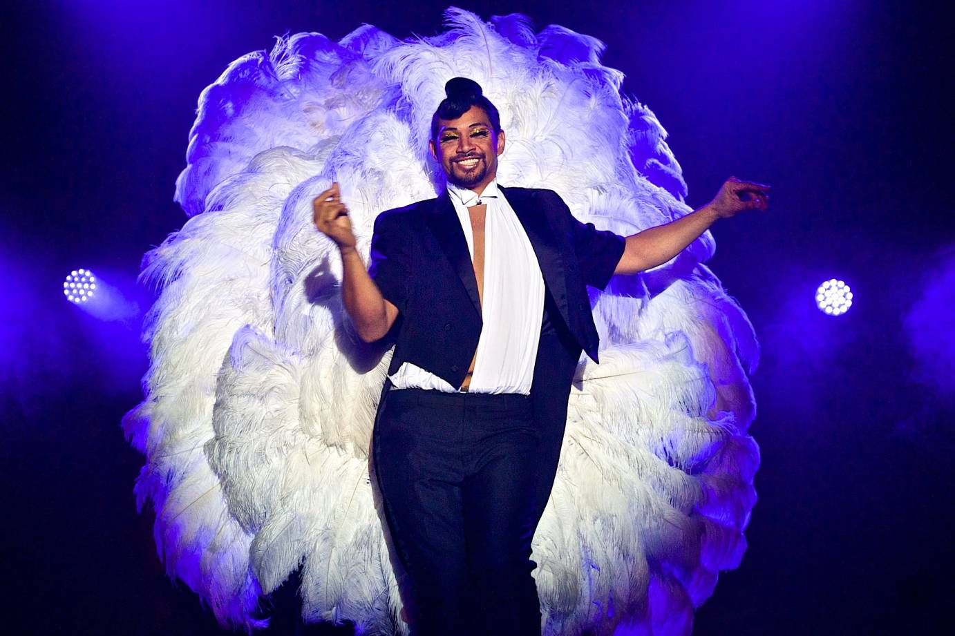 A bearded man in a suit and showgirl feathers